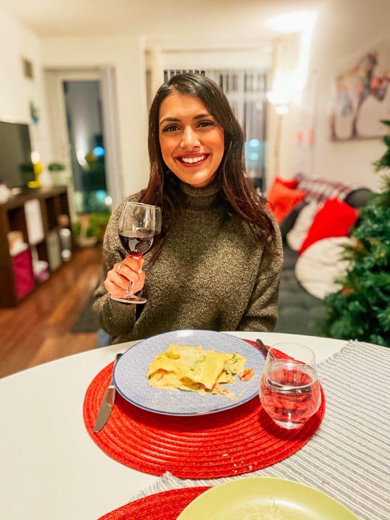 Woman smiling and holding a glass of red wine with a meal she created through cooking classes. 