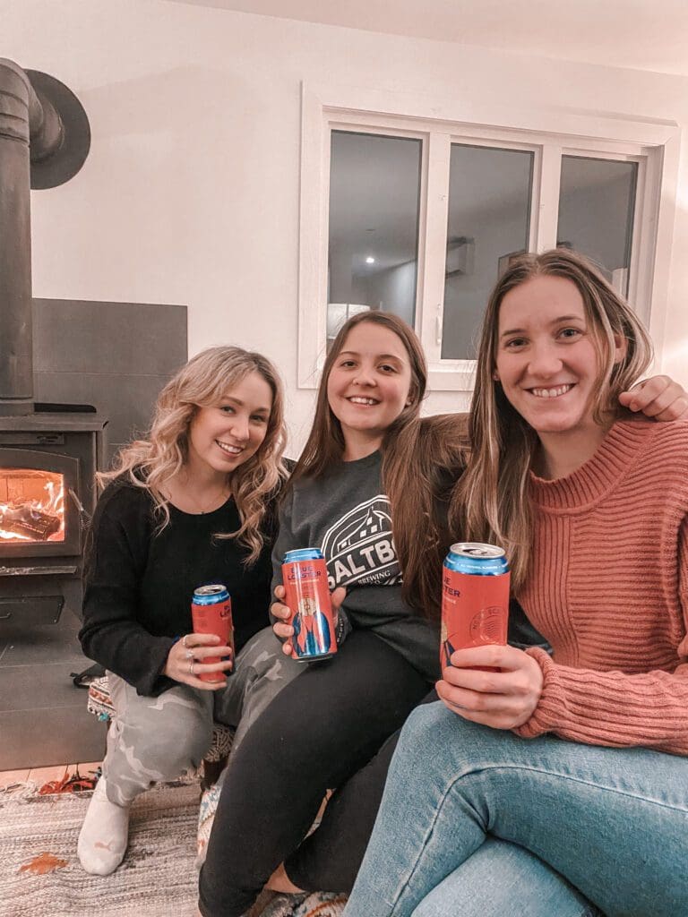 A group of smiling women hanging out in front of a fireplace in the living room of a luxury staycation.