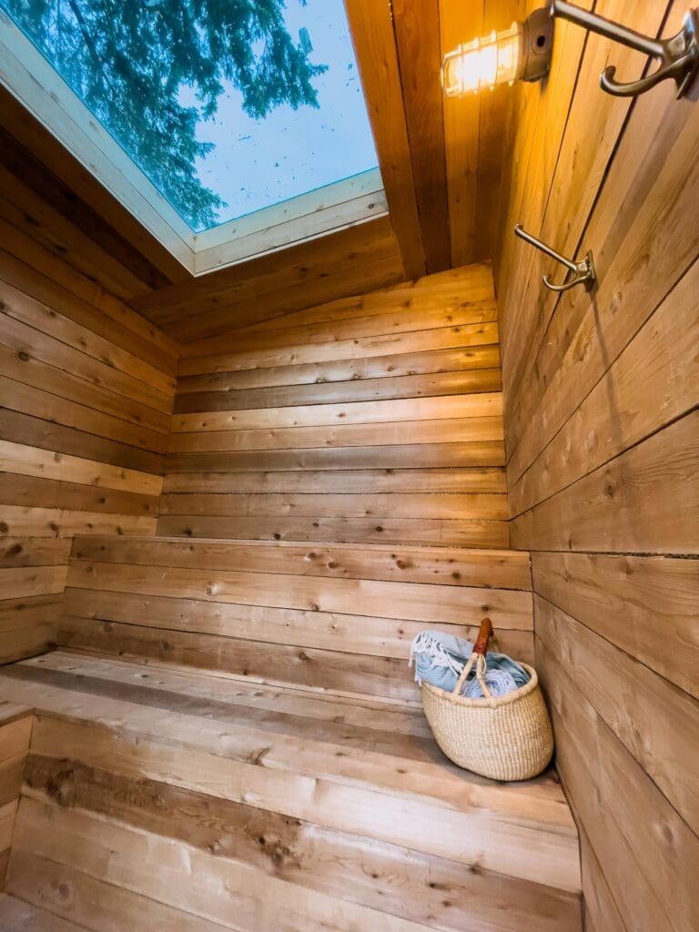 Inside the sauna at Tin Can Ranch. There is a small straw bag with towels and a huge skylight in the top. The back wall has two levels of benches.