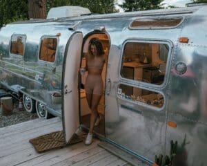A girl is walking out of the Tin Can Ranch Airstream. It is almost dark out as the sun is going down. The airstream is very shinny.