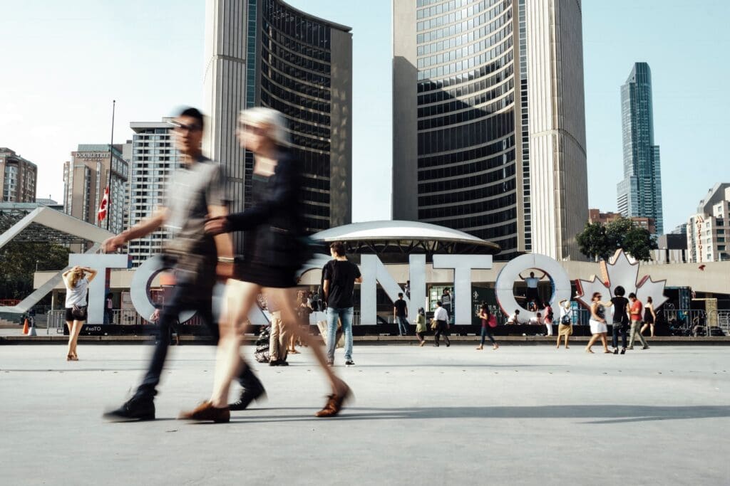 People walking past a large TORONTO sign in Nathan Philip's Square