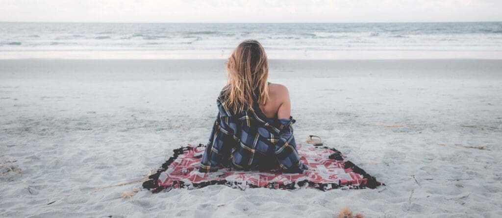 A girl sitting on the beach facing the ocean on a solo date night