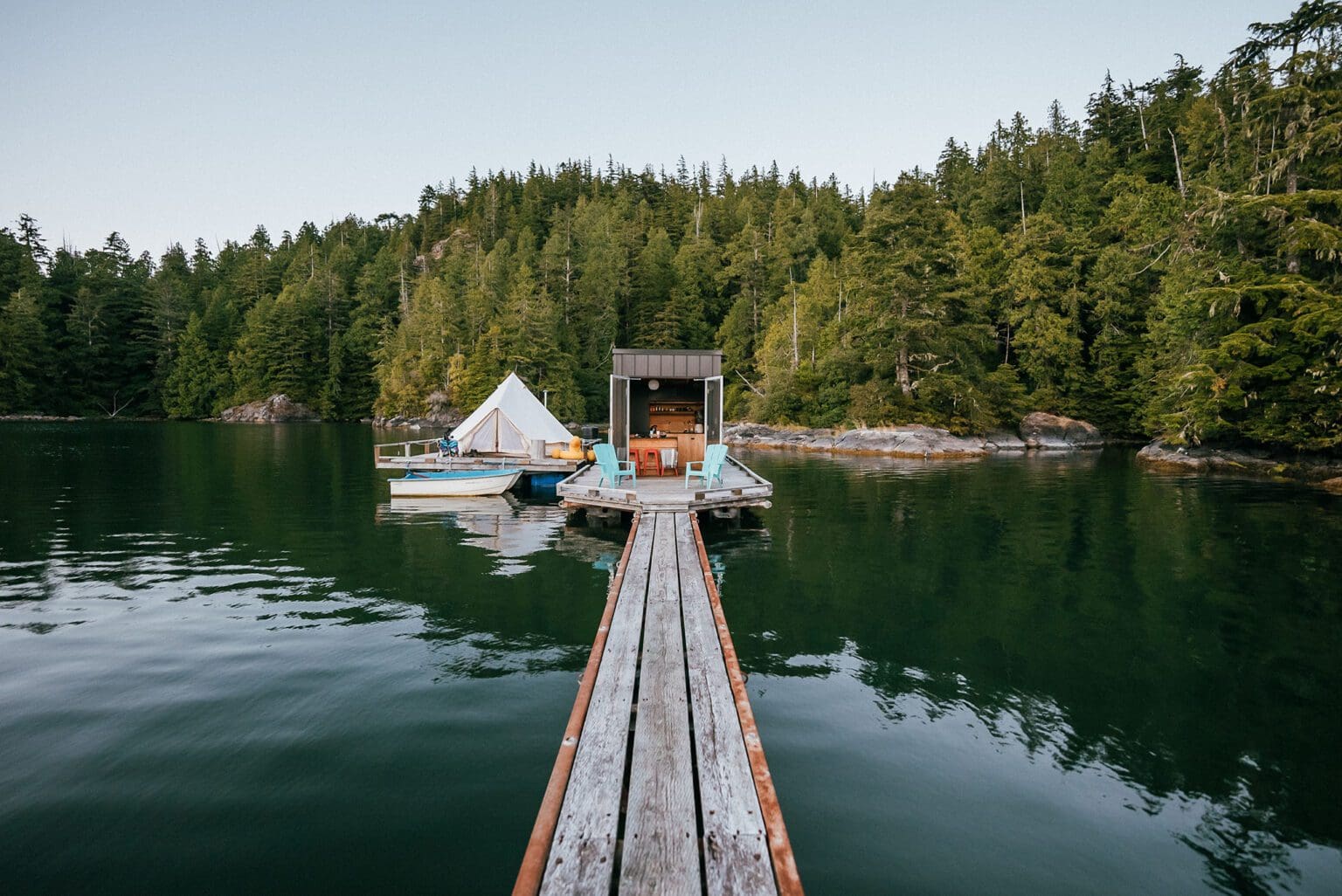 The lagoon float camp in Tofino British Columbia. The water is calm, the sky is blue and you are looking down the dock into the float camp.
