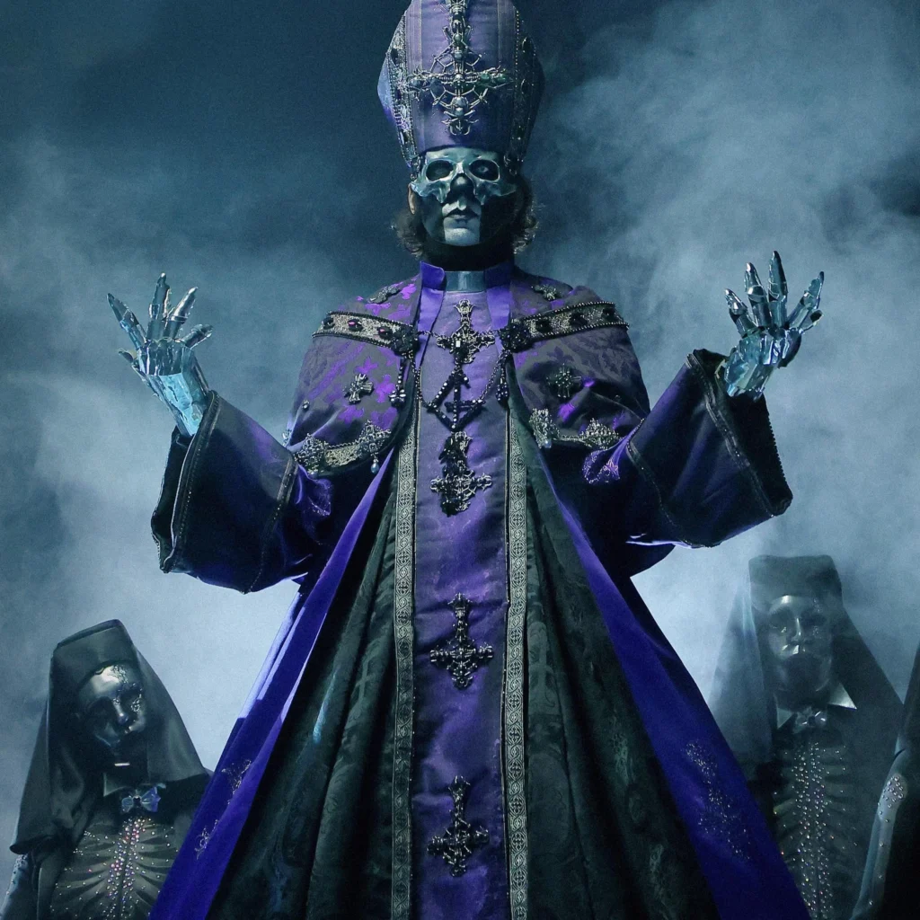 The band Ghost dressed as a metal skeleton in purple priest clothing with two skeleton nuns behind, with a dark background and white smoke all around