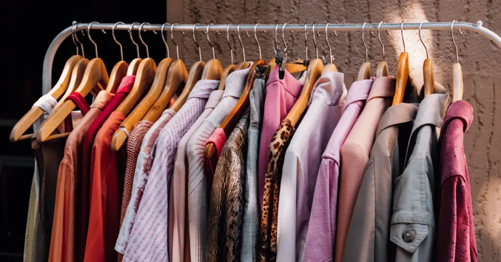 shirts, sweaters, and jackets hanging on a white clothing rack behind a brown/tan cement background