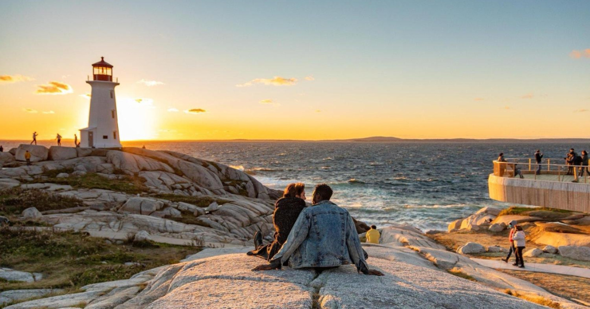 a couple sitting on a rock looking over the ocean in halifax at sunset