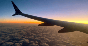 airplane wing flying above the clouds with an orange sunset