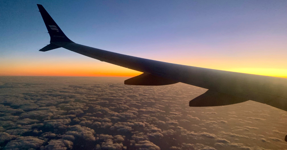 airplane wing flying above the clouds with an orange sunset
