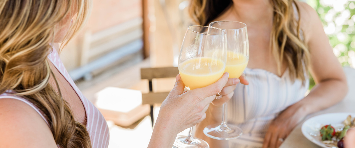 An image of two smiling women clinking their mimosas together on a boozy brunch date.