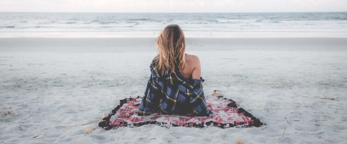 A girl sitting on the beach facing the ocean on a solo date night