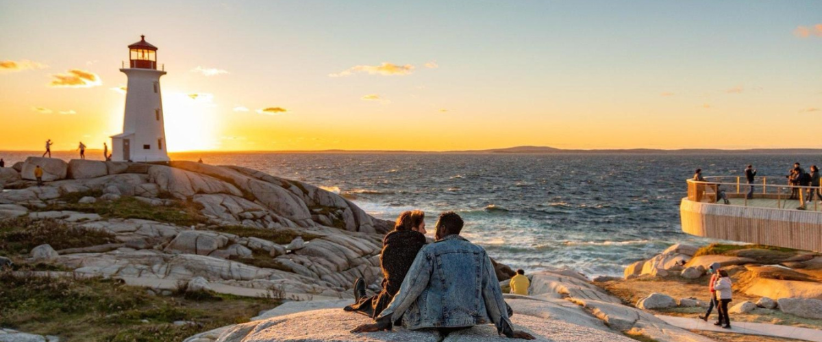 a couple sitting on a rock looking over the ocean in halifax at sunset