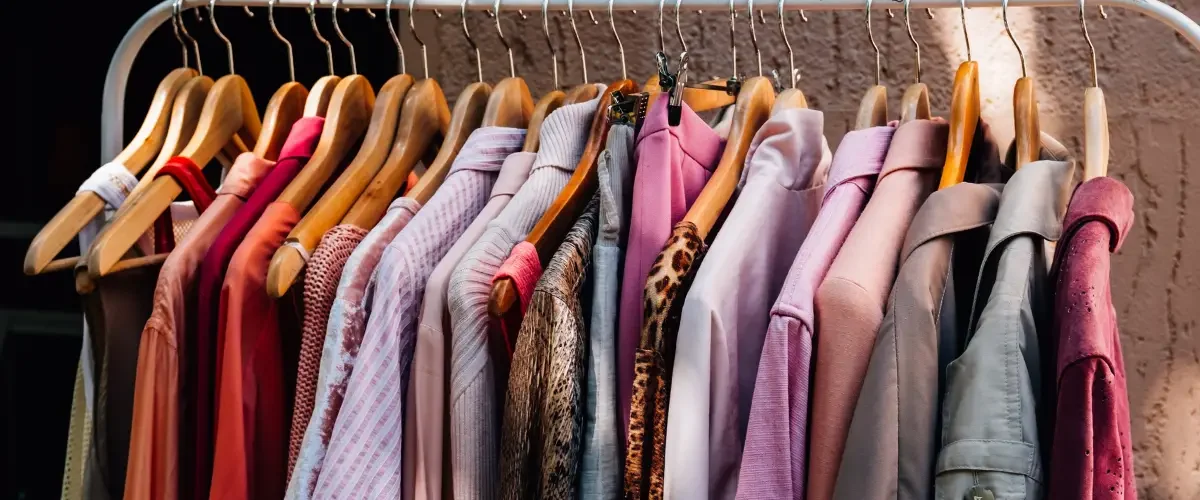 shirts, sweaters, and jackets hanging on a white clothing rack behind a brown/tan cement background