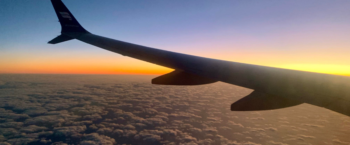 airplane wing flying above the clouds with an orange sunset
