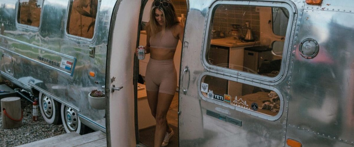 A girl is walking out of the Tin Can Ranch Airstream. It is almost dark out as the sun is going down. The airstream is very shinny.