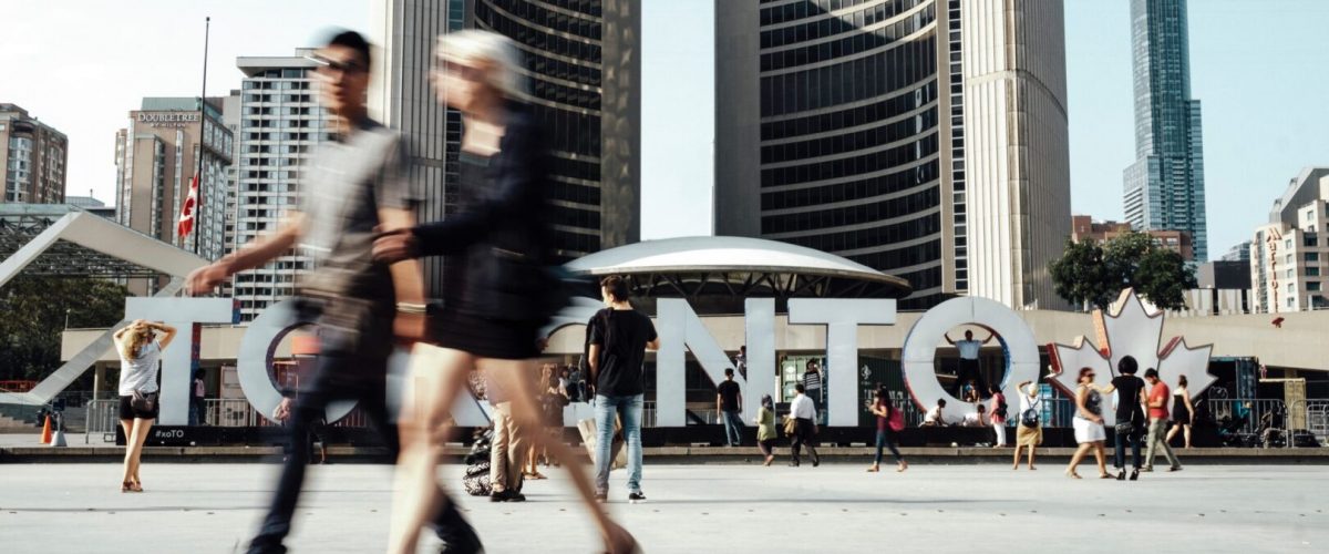 People walking past a large TORONTO sign in Nathan Philip's Square