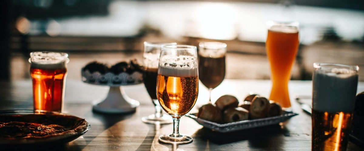 Different glasses of beer on a patio table with a very blurry background lake.The sun is just about to set.