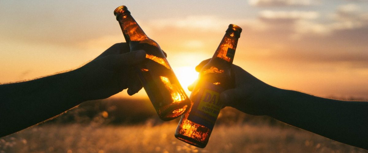 Two beers clinking together in front of a sunset.